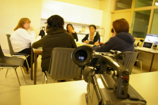 Photo of women chatting around a table with a camera filming them